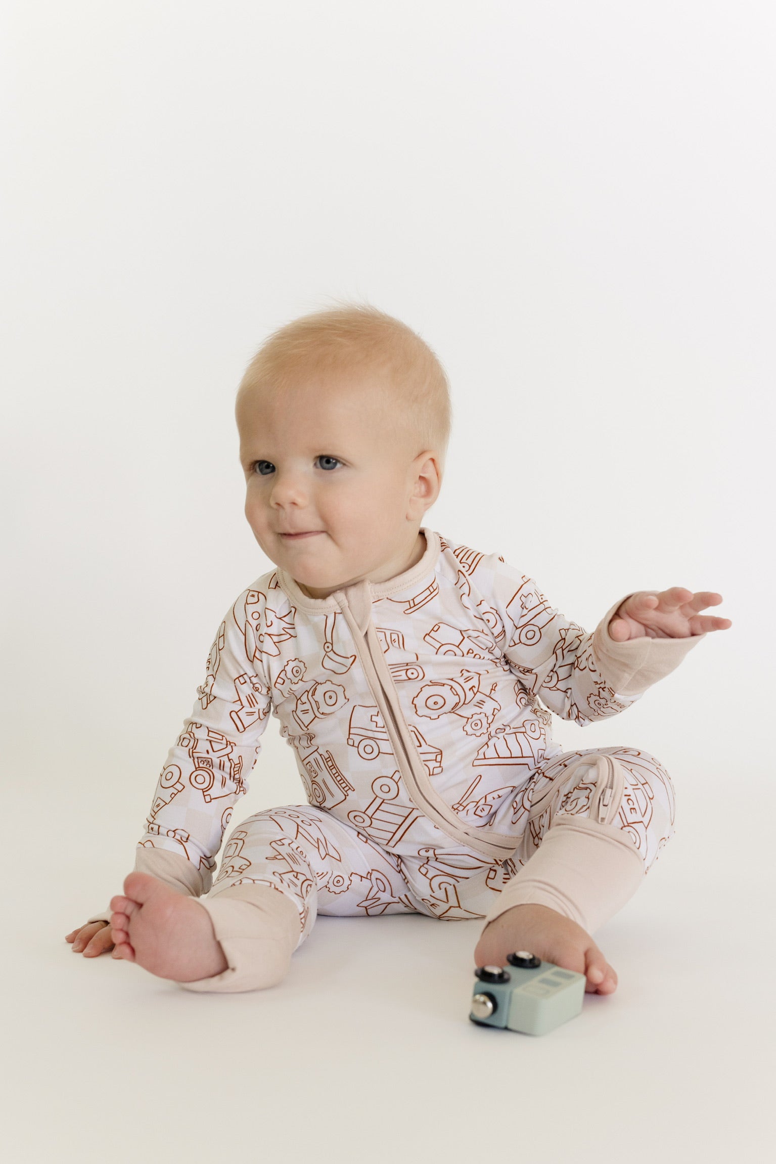Baby wearing a patterned onesie sitting on a white surface